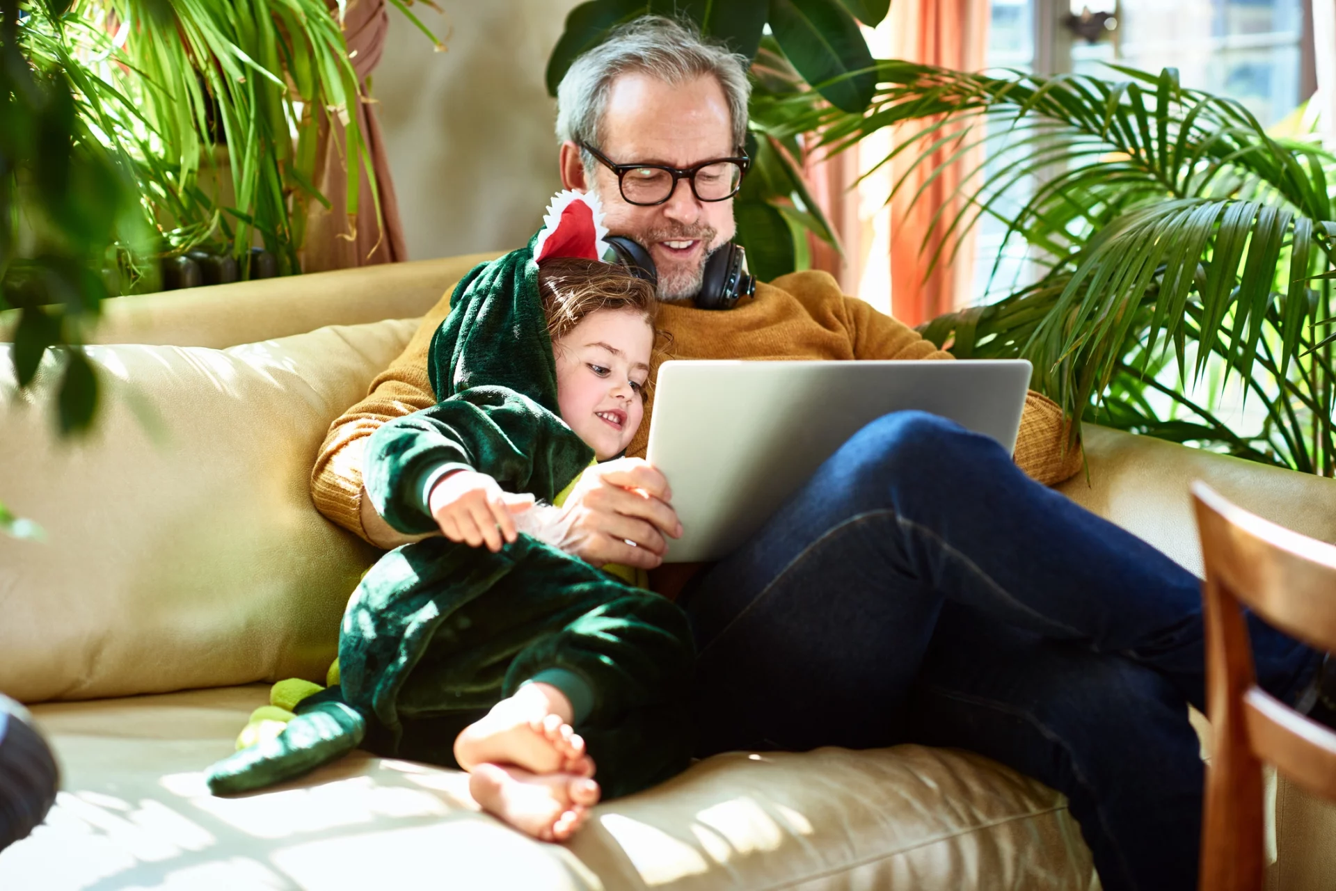 Homem faz uso de computador do lado de filha ou neta pequena, que sorri para o que ele está vendo