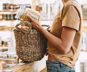 Mulher coloca macarrão a granel em pote de vidro dentro de cesto de palha no dia do consumo consciente