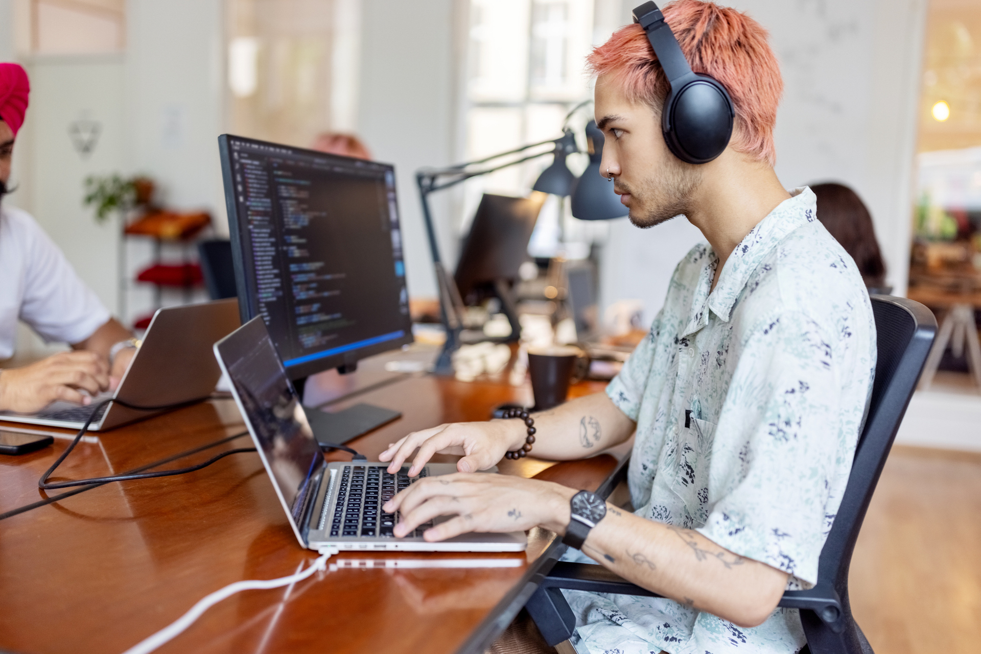 Jovem mexe com dois computadores enquanto ouve música no headphone porque a computação é uma das profissões em alta