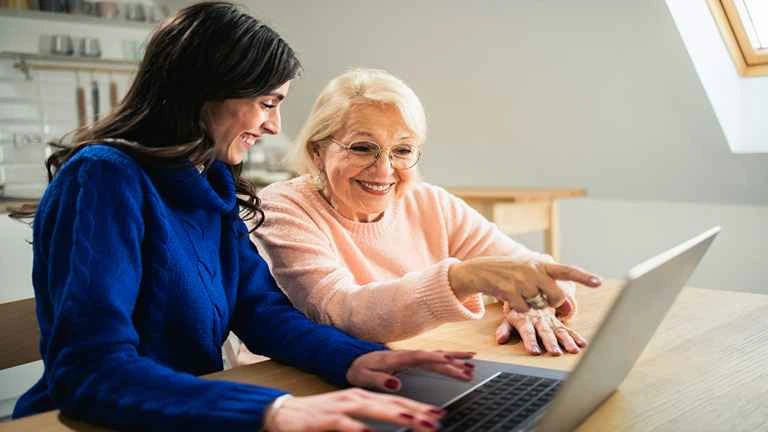 Mulher auxilia senhora com a tecnologia, ela faz trabalho voluntário possibilitando que a senhora saiba navegar on line 