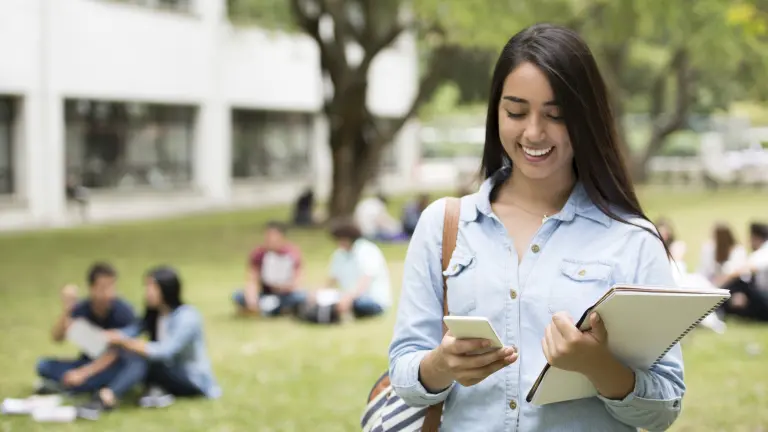 Imagem mostra jovem sorridente conferindo notícias no celular. Ela está animada pela proximidade das eleições