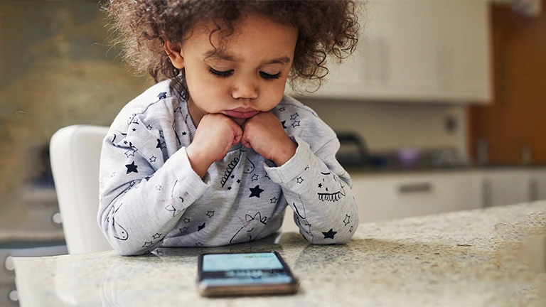 Criança pequena assiste concentrada a algum conteúdo no celular. 