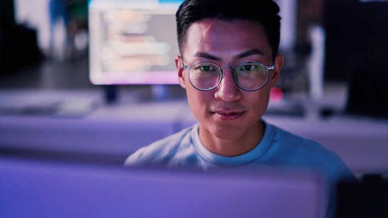 Homem oriental trabalha focado no seu computador. Ele é um profissional de cibersegurança.