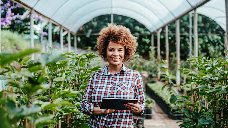 Mulher segurando um tablet diante do seu cultivo sorri por ser uma das mulheres do agro que estão fazendo a diferença no país