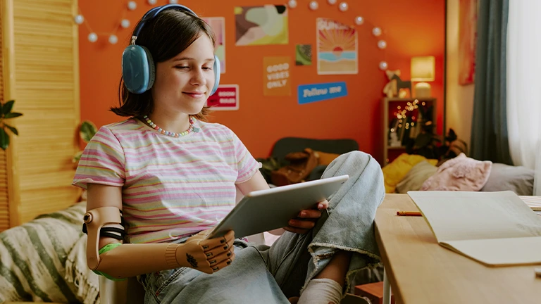 Jovem com deficiência visual e uma prótese no braço direito usa o seu tablet sorrindo por causa dos mecanismos que permitem a acessibilidade