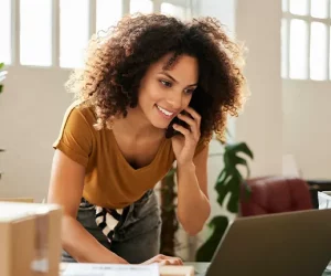 Mulher negra empreendedora fala ao telefone enquanto confere computador para enviar o pedido o quanto antes para a celebração do dia da consciência negra