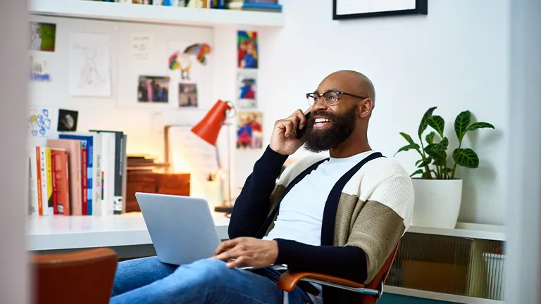 Homem negro empreendedor sorri ao falar no telefone com contato que conseguiu no computador para fechar o negócio 