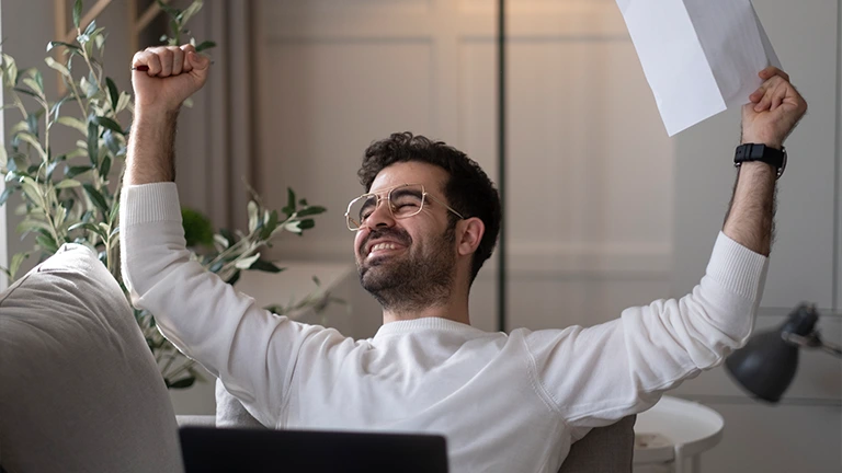 Homem celebra com computador no colo e um boleto na mão, porque graças a lei do superendividamento ele conseguiu quitar as suas contas