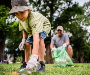 Criança pega garrafa plástica e pai ao fundo sorri, orgulhoso do filho