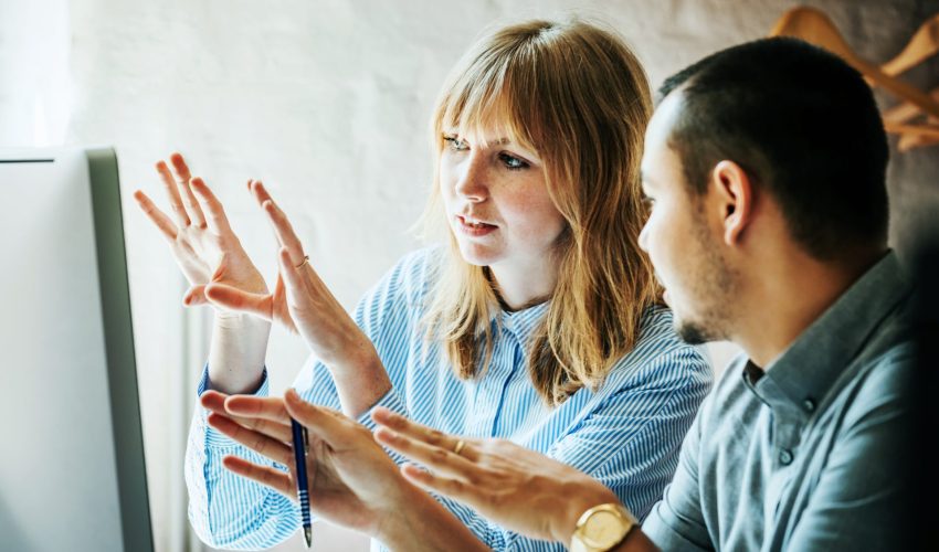 Colegas de trabalho pensam, juntos, na frente do computador, sobre uma melhor forma de criar o projeto na empresa