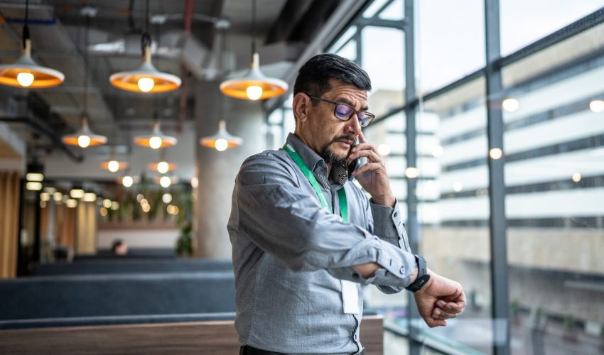 Homem olha relógio enquanto está no telefone para fazer a sua gestão do tempo entre o que precisa ser feito e o horário que tem disponível