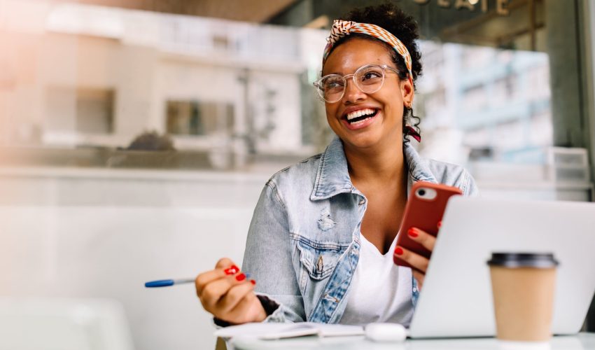 Mulher sorri com celular na mão enquanto percebe que tem tido sucesso no uso da tecnologia para aprimorar suas habilidades pessoais
