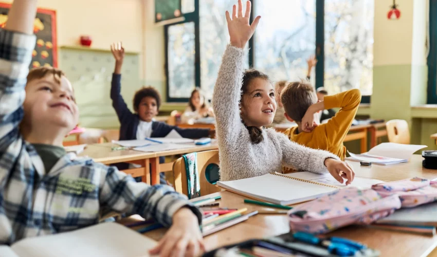 Crianças na escola levantam a mão para responder a pergunta da professora