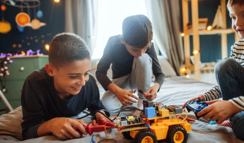 Três meninos constroem, juntos e felizes, o brinquedo eletrônico deles: um carrinho de controle remoto