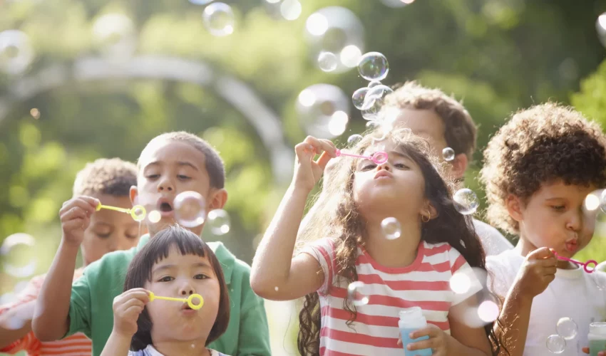 Grupo de crianças brincando com bolhas de sabão em um ambiente ao ar livre com muita luz e vegetação verde