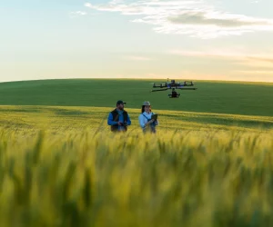 Dois agricultores em campo de trigo utilizando drone para otimizar recursos naturais e monitorar a plantação ao pôr do sol