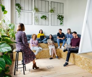 Mulher reforça aprendizados que a educação corporativa pode ter na empresa, e funcionários a escutam com atenção