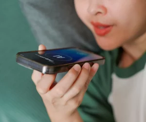 Close de uma pessoa falando ao celular com a interface de IA ativada na tela, utilizando a lei do esforço mínimo para realizar tarefas por voz.