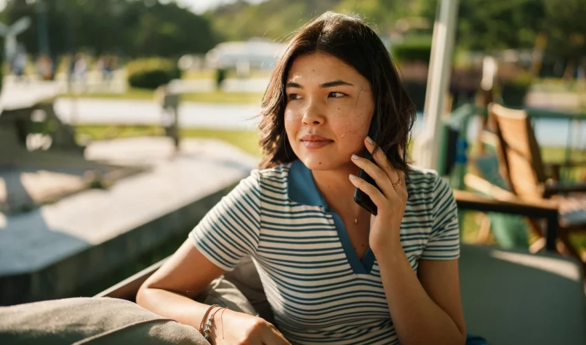 Mulher jovem falando ao celular em um parque, representando o recebimento de chamadas telefônicas que podem ser golpes de IA.