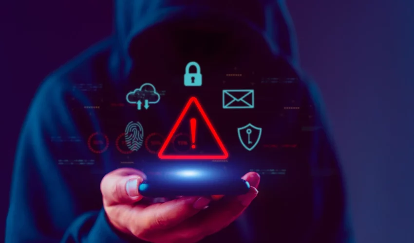 Hacker segurando celular com ícones de segurança cibernética e um sinal de alerta vermelho brilhante, simbolizando crimes virtuais com IA.