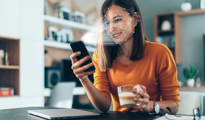 Mulher usando smartphone com interface gráfica de reconhecimento facial (malha de pontos) sobre o rosto, representando segurança digital.