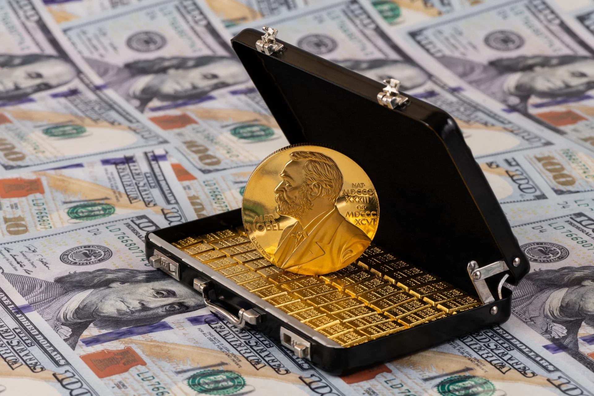 Uma réplica da medalha de ouro do Prêmio Nobel dentro de uma maleta pequena com barras de ouro, sobre um fundo de notas de dólares.